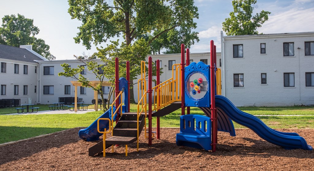a playground with a blue and red playset in front of a building