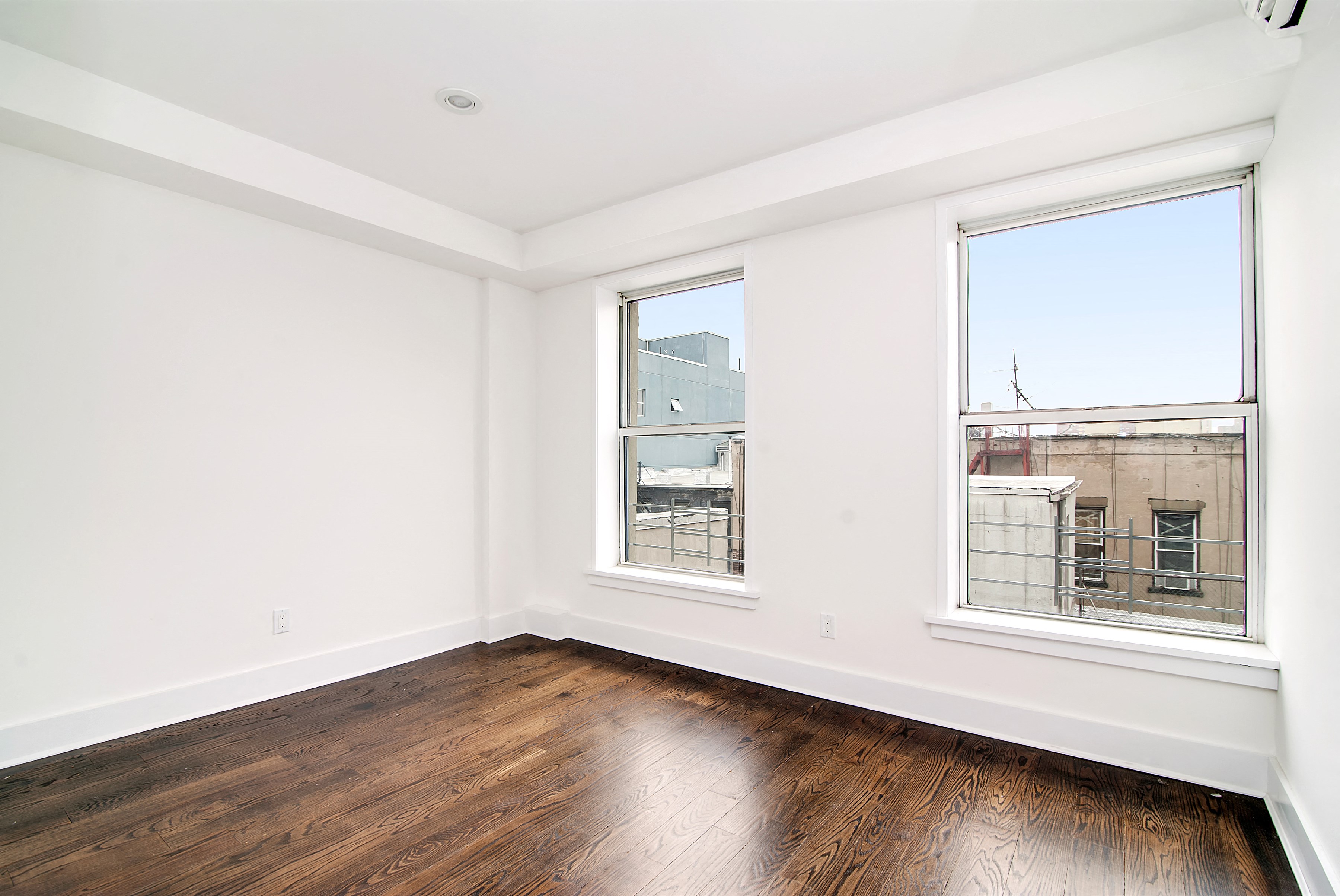 an empty room with hardwood floors and two windows