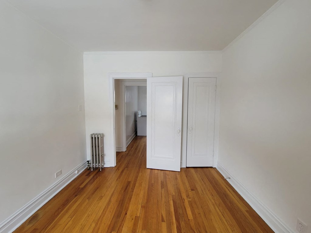 a bedroom with white walls and wood floors and a closet