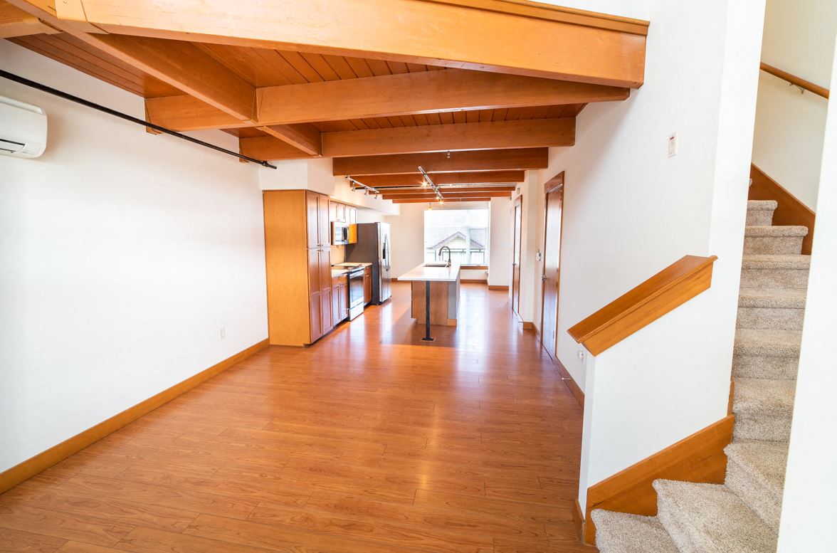 a hallway with wood floors and white walls and a staircase