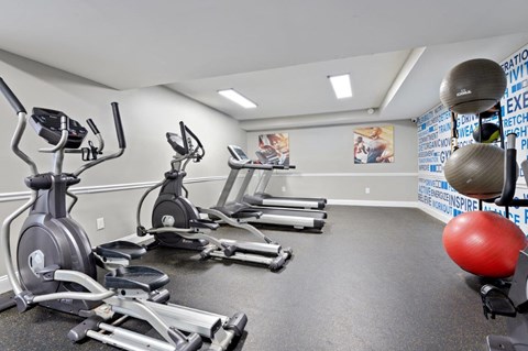 A gym with a row of treadmills, elliptical machines, and a red exercise ball.