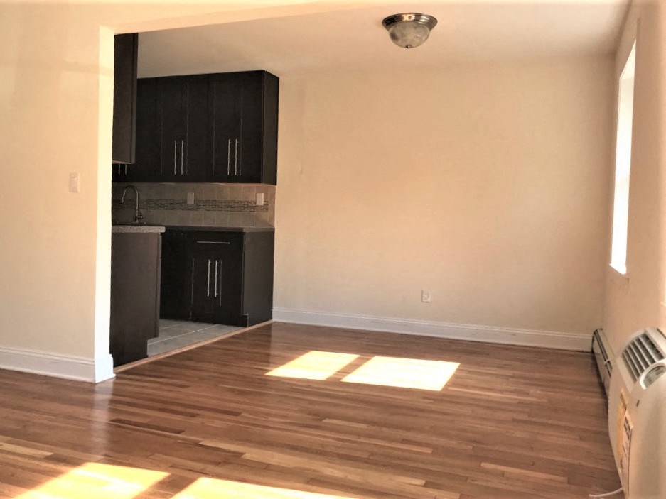 an empty living room with wooden floors and a kitchen