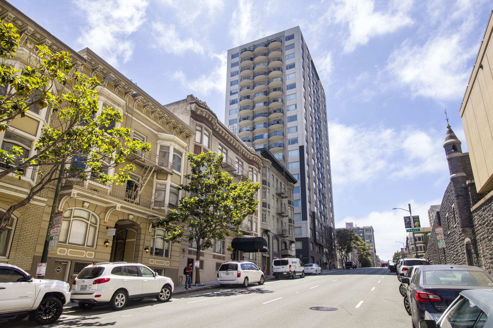 A street view with cars parked on the side and a tall building in the background.