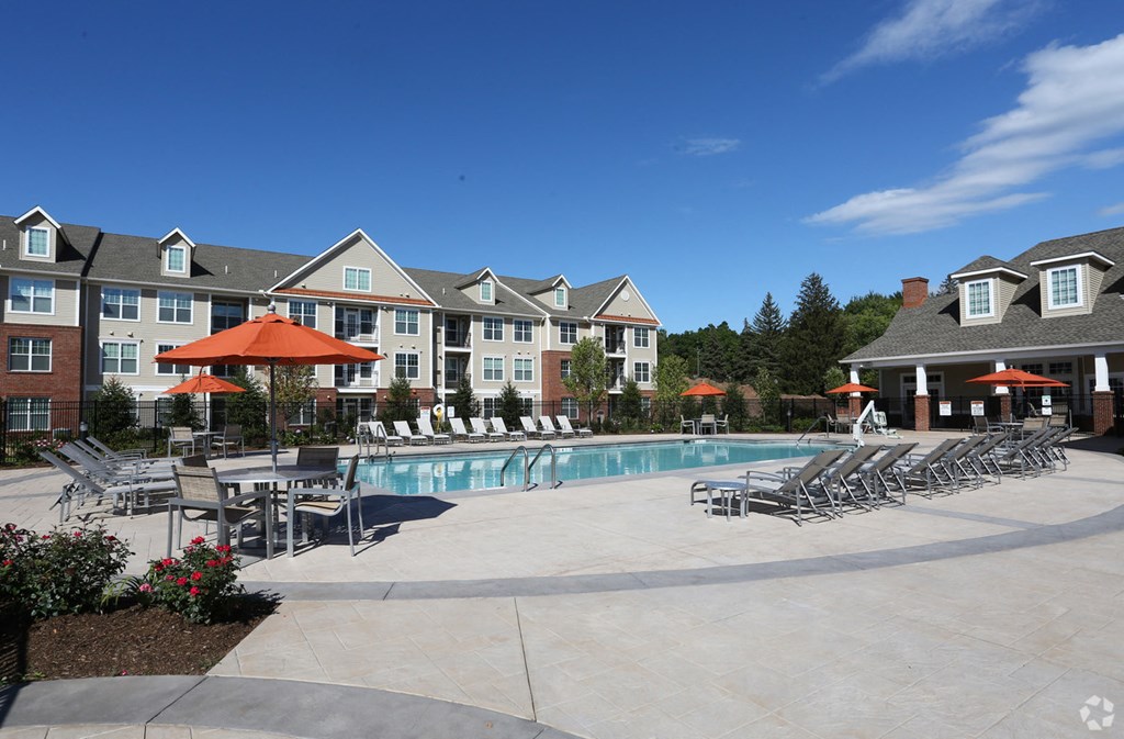 a swimming pool with chairs and umbrellas in front of an apartment building