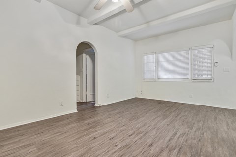 A room with a wooden floor and a white wall with a doorway leading to another room.