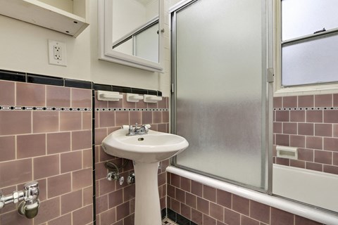 A white pedestal sink in a bathroom with pink tiles.