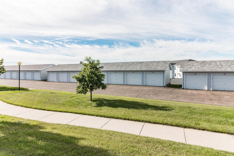 a row of white garages with a sidewalk and grass