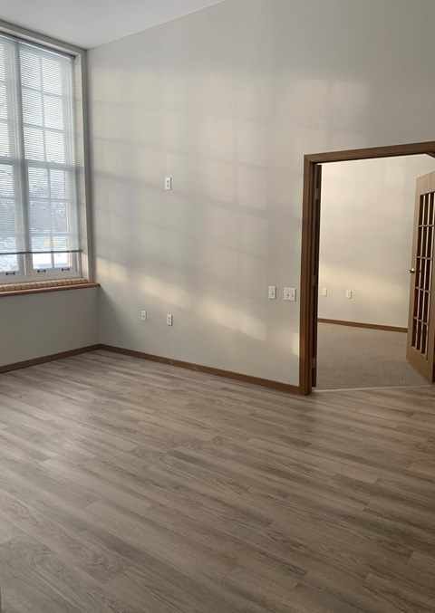 an empty living room with wood floors and a door to a bedroom