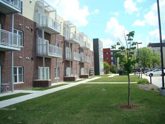 a row of brick apartment buildings with green grass and a sidewalk