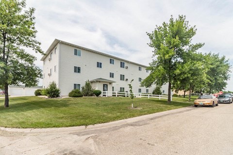 the exterior of a white apartment building with cars parked in front