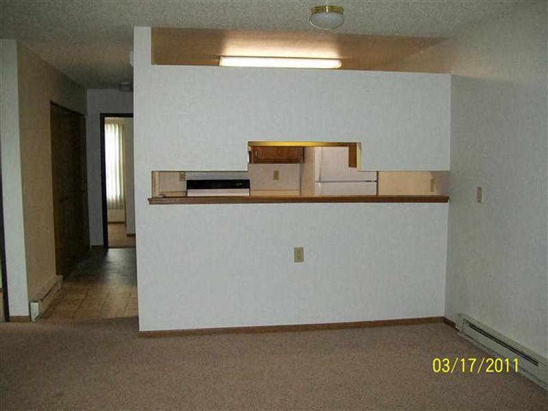 an empty living room with a white wall and a kitchen