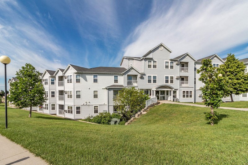 a large white apartment building on a hill with grass and trees