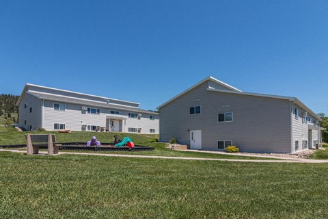 two houses with people sitting on a hammock in the grass