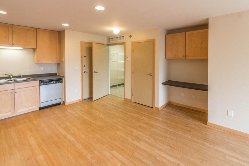 an empty kitchen and living room with wood flooring and a door to a bathroom