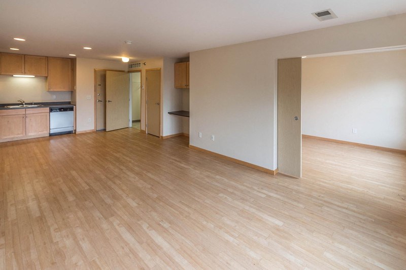 an empty living room with wood flooring and a kitchen
