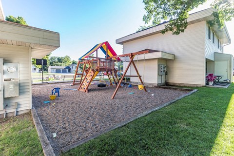 A playground with a slide and swings is in front of a house.