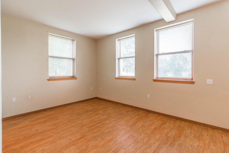 an empty room with a wood floor and three windows