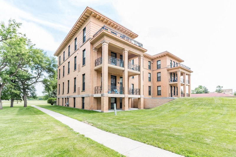 a building on the side of a green lawn and a sidewalk