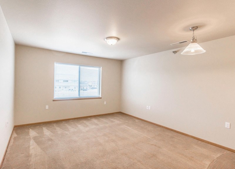 the living room of an empty home with a large window and carpet