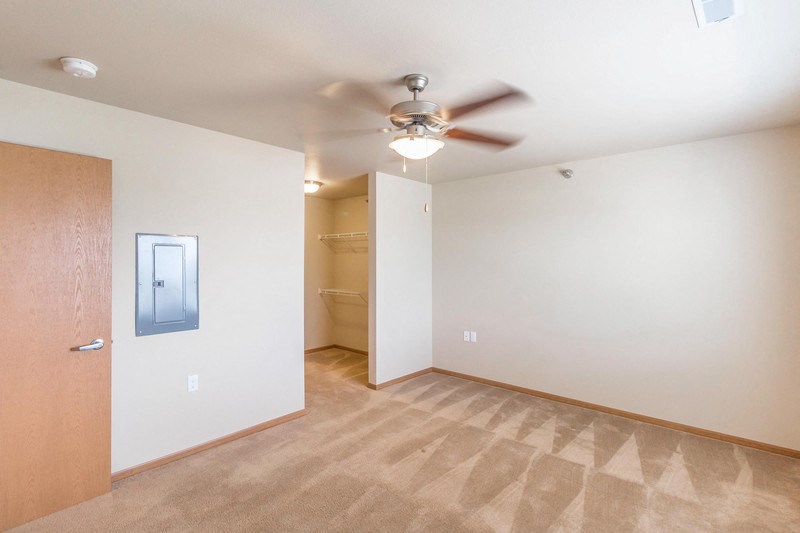 an empty living room with a ceiling fan and a closet