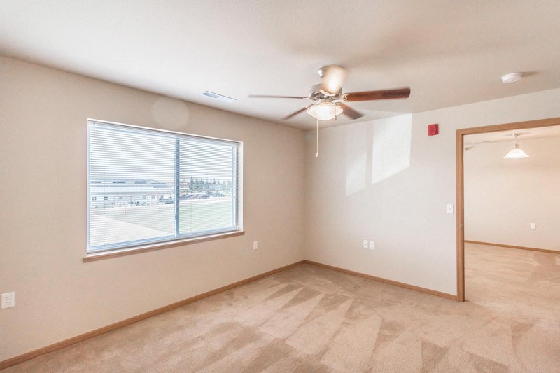 the spacious living room with a large window and a ceiling fan