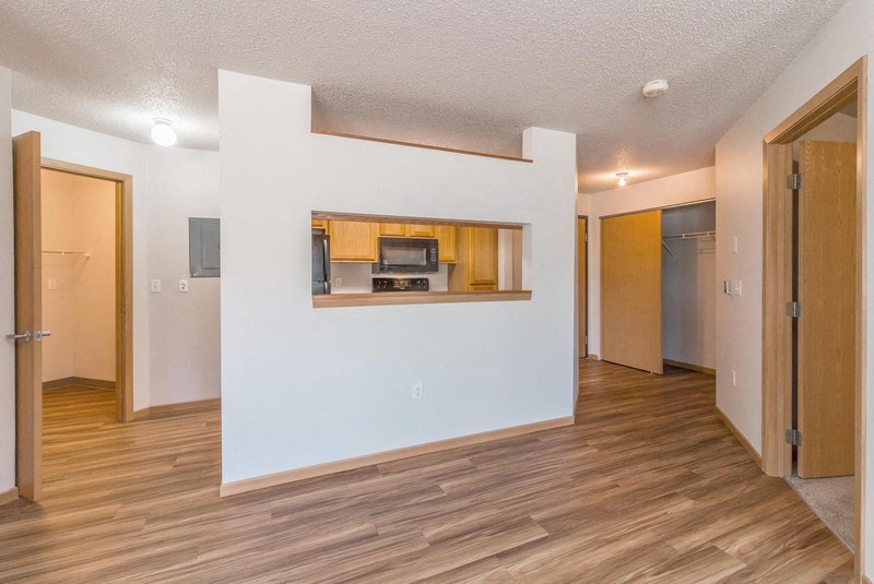 the living room and kitchen of an apartment with a wood floor and white walls
