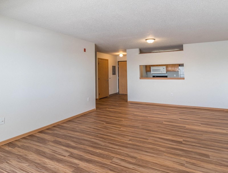 the living room and kitchen of an empty apartment with wood flooring