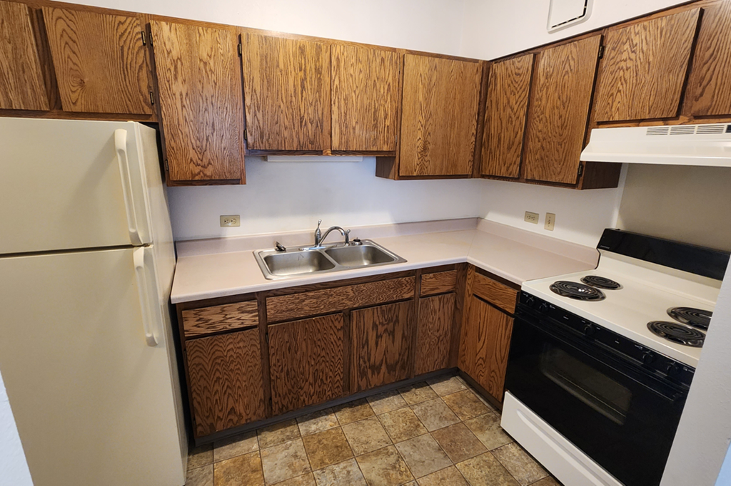 an empty kitchen with wooden cabinets and a stove and refrigerator