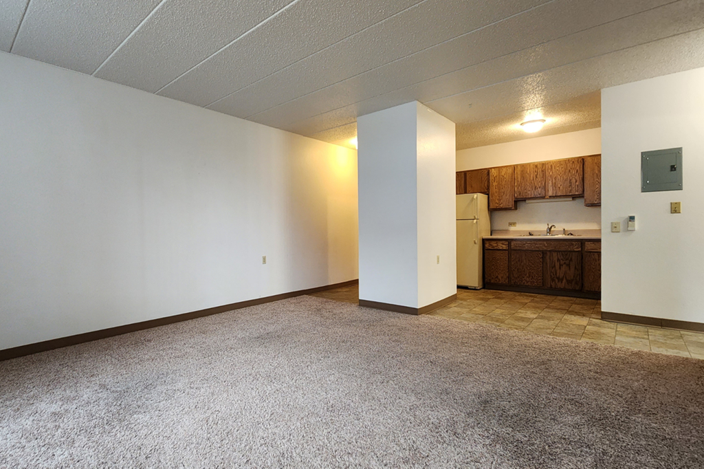 an empty living room with a kitchen in the corner