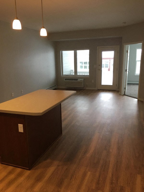 an empty living room with a kitchen and wood floors