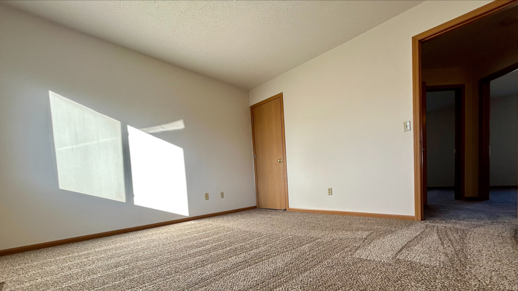an empty living room with carpet and a door to a bedroom
