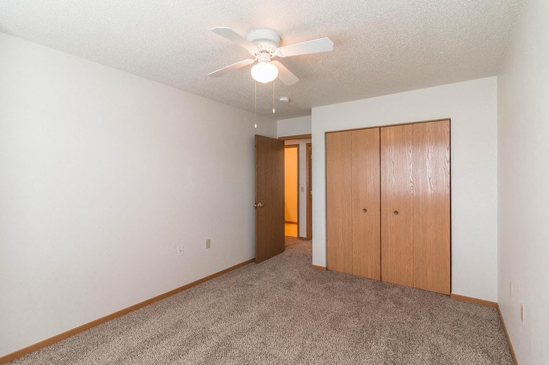 an empty living room with a ceiling fan and closet