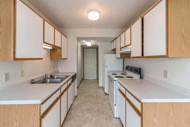 an empty kitchen with white counters and wooden cabinets and a white refrigerator