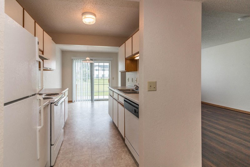 an empty kitchen with white appliances and a door to a balcony
