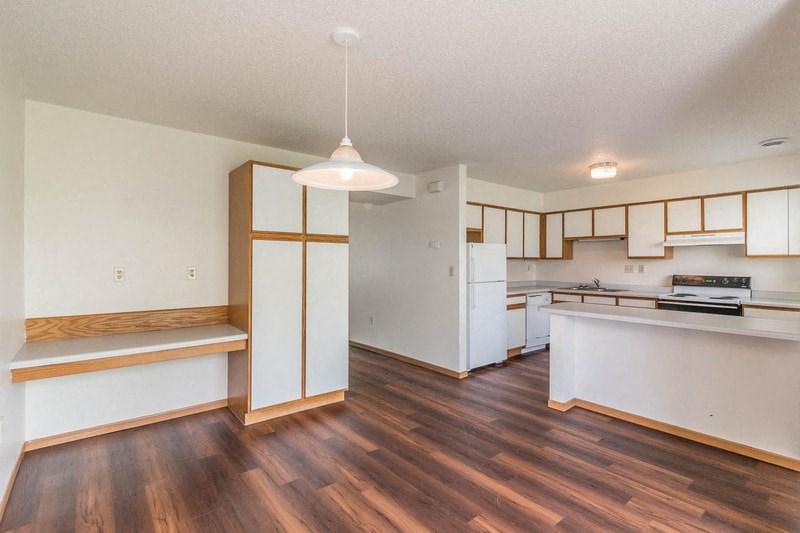 an empty kitchen with white appliances and wood floors