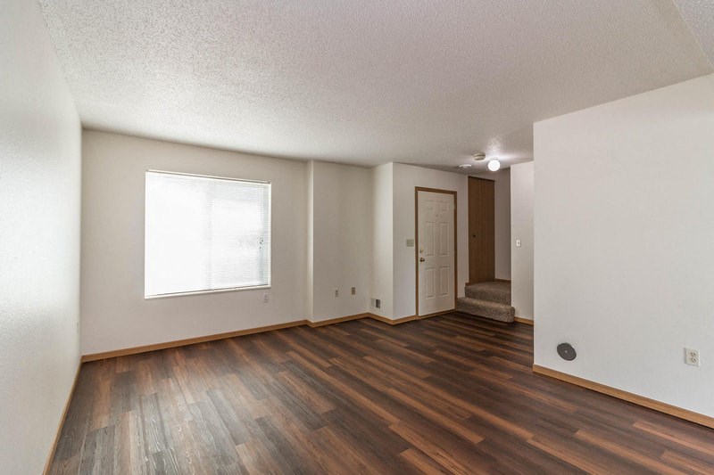 an empty living room with hard wood flooring and a window
