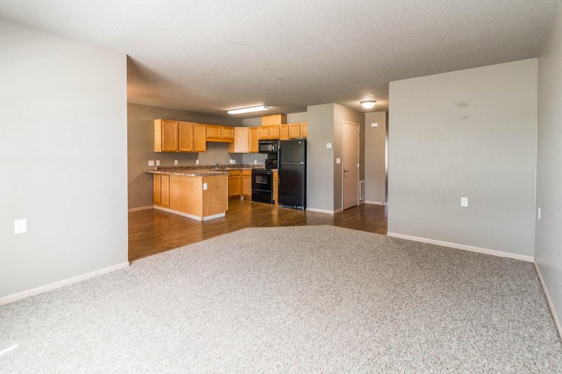 an empty living room and kitchen with wood cabinets