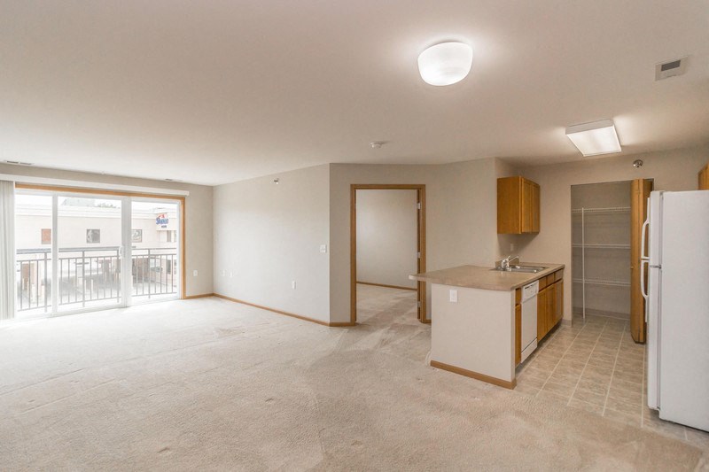 an empty living room with a kitchen and a door to a balcony