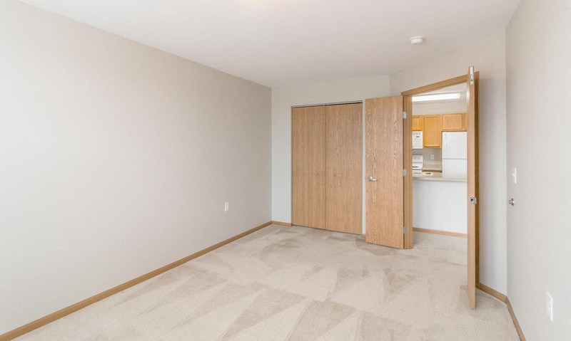 an empty room with a door to a kitchen and a closet