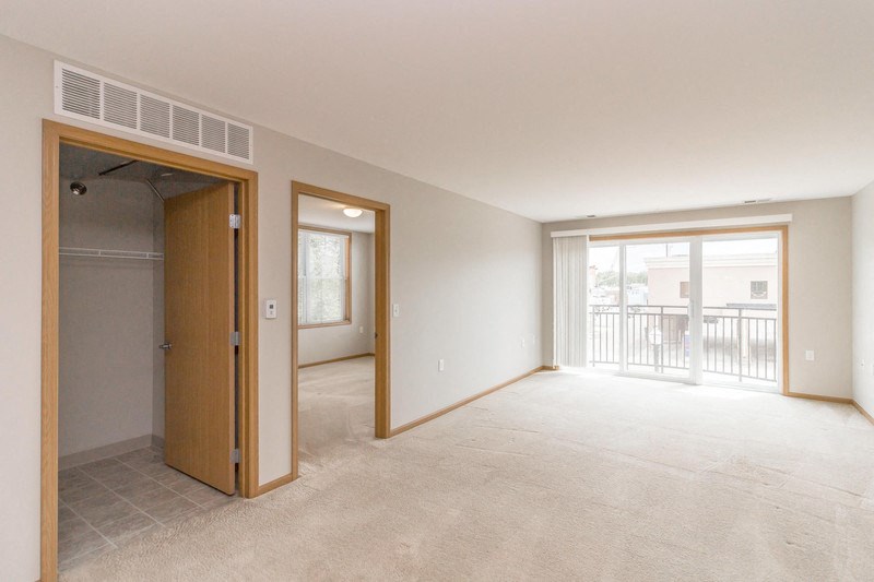 the living room and bedroom of an empty apartment with a door to a balcony