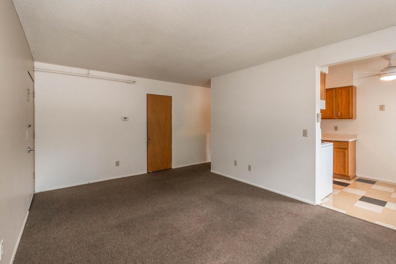an empty living room with carpet and a door to a kitchen