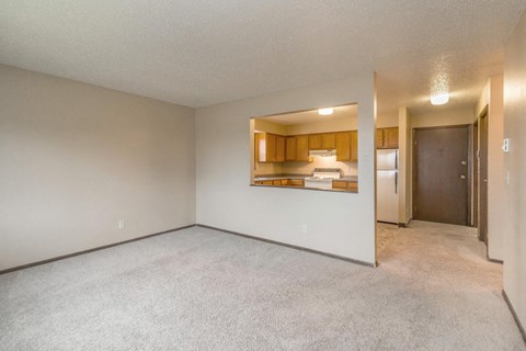 an empty living room with a kitchen in the background