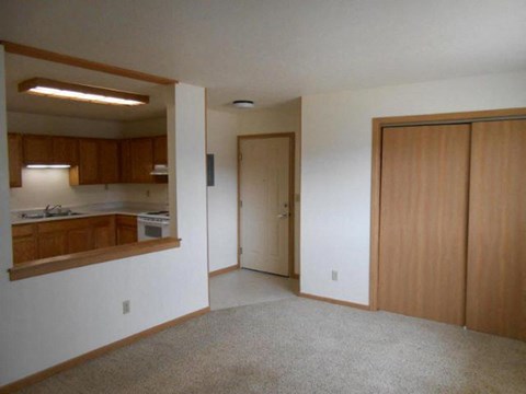 an empty living room with a kitchen and a door