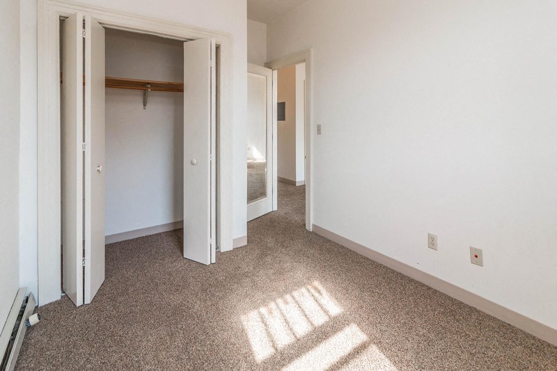an empty room with a hallway to a bedroom and a closet