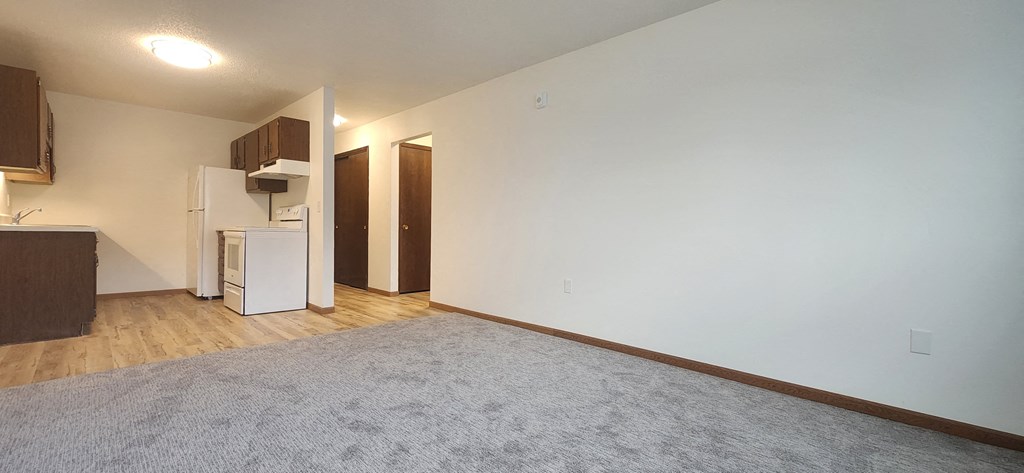 an empty living room and kitchen with white walls and wood floors