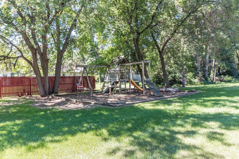 a playground in a yard with trees and a swing set