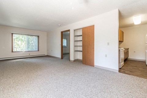 an empty living room with a kitchen and a window