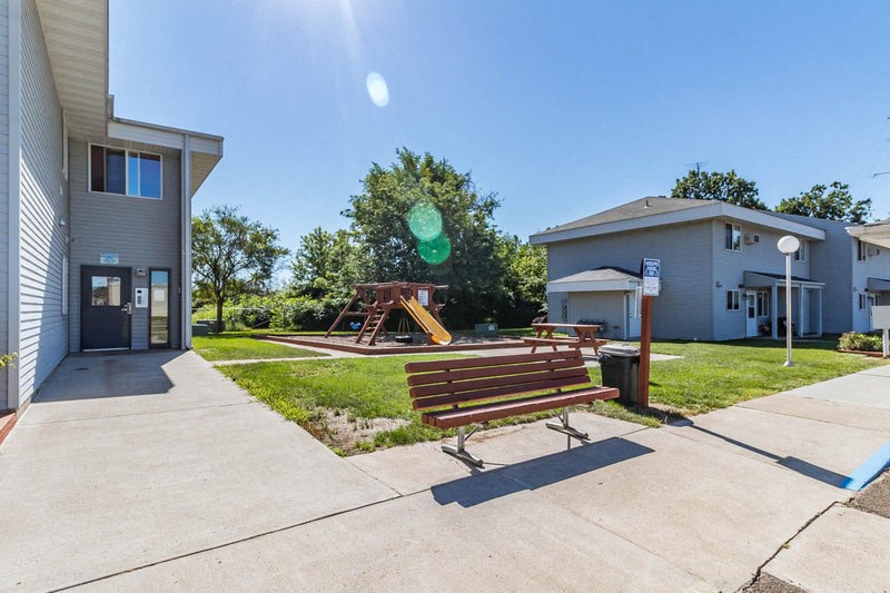 a sidewalk with a bench and a playground in front of a building