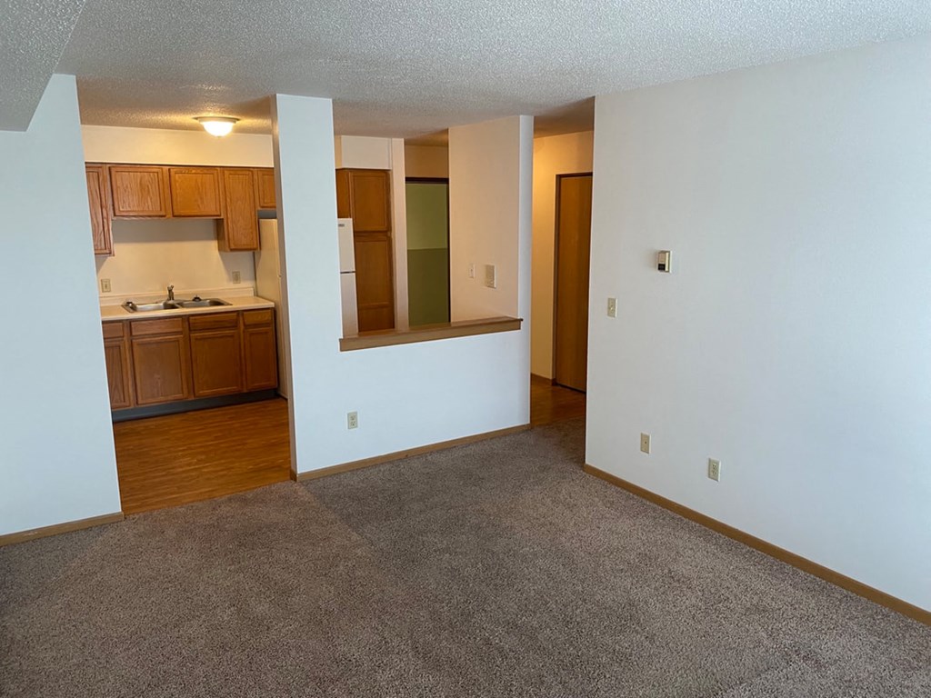 an empty living room and kitchen with wood floors and white walls