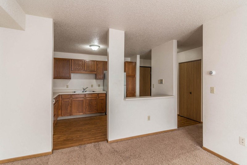 an empty living room and kitchen with wood flooring and white walls